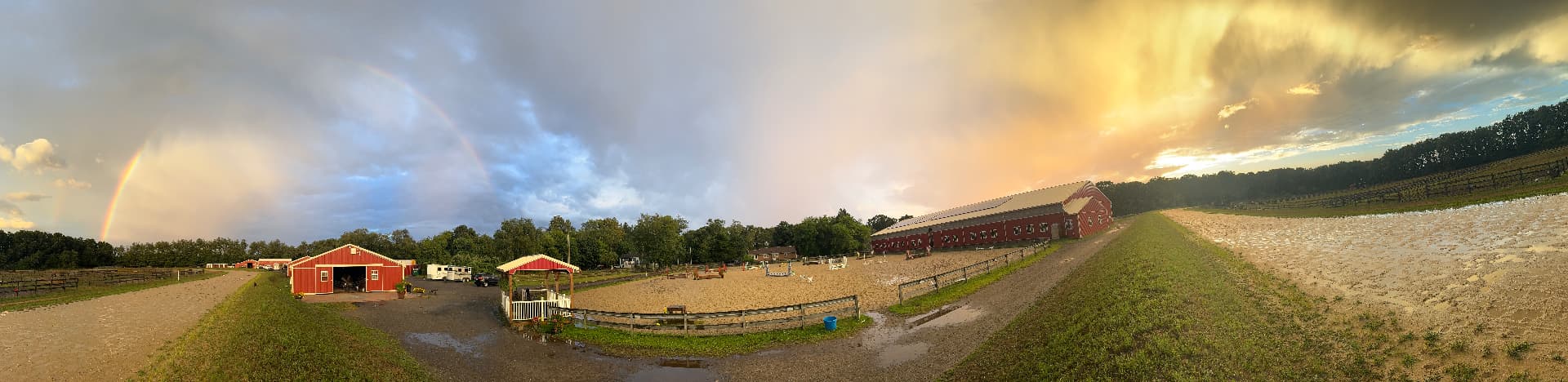 Panoramic rainbow view across the red barns, outdoor jumping arena and sand track at Posnerosa