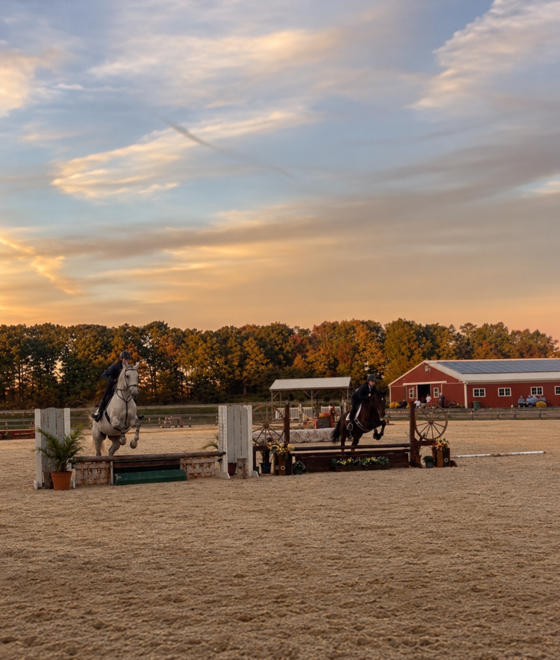 Two riders jumping a grey horse and a dark horse over hunter fences in the Posnerosa outdoor arena beneath a golden evening sky