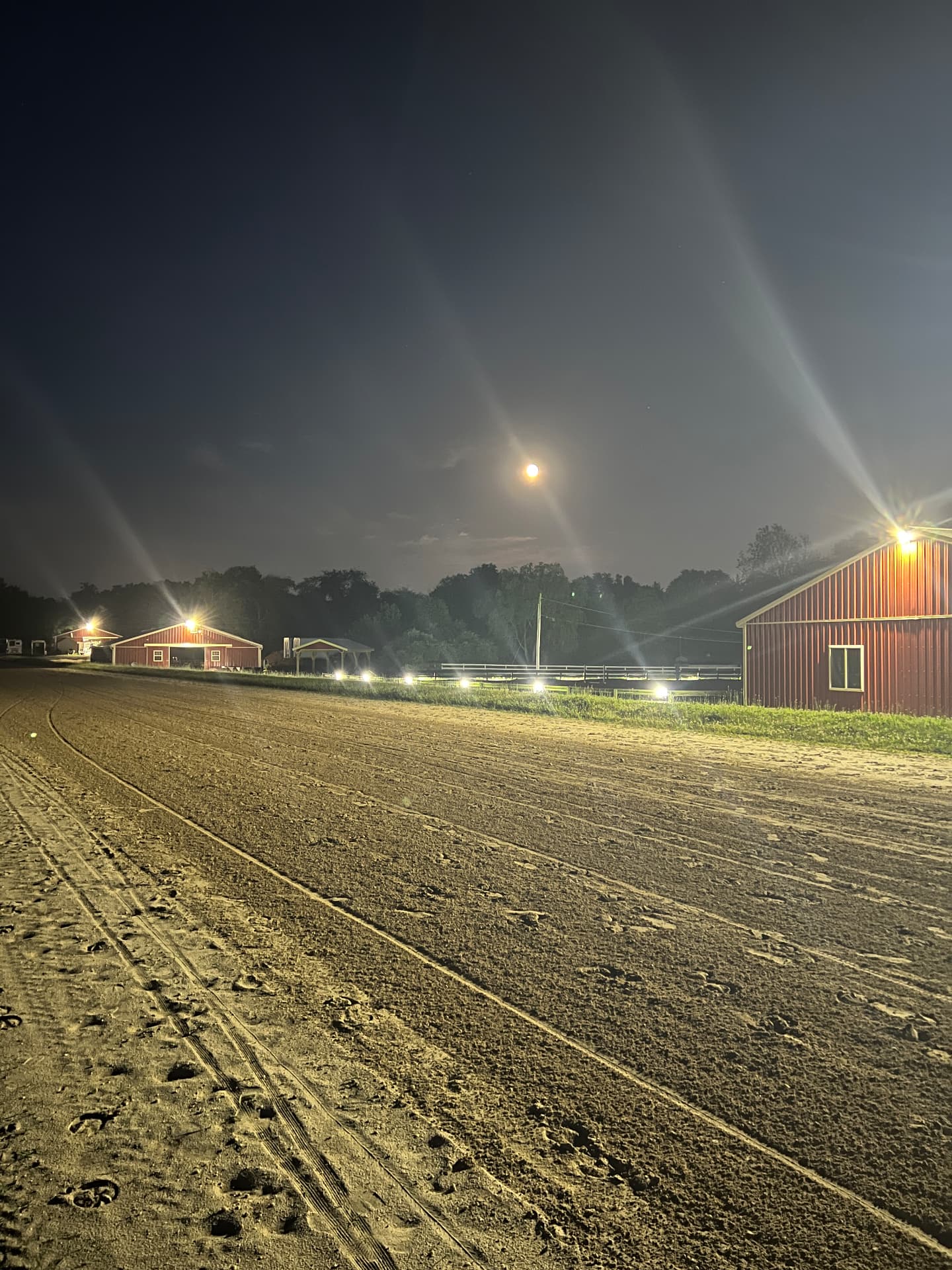 Moon above the illuminated sand track and red barns at Posnerosa