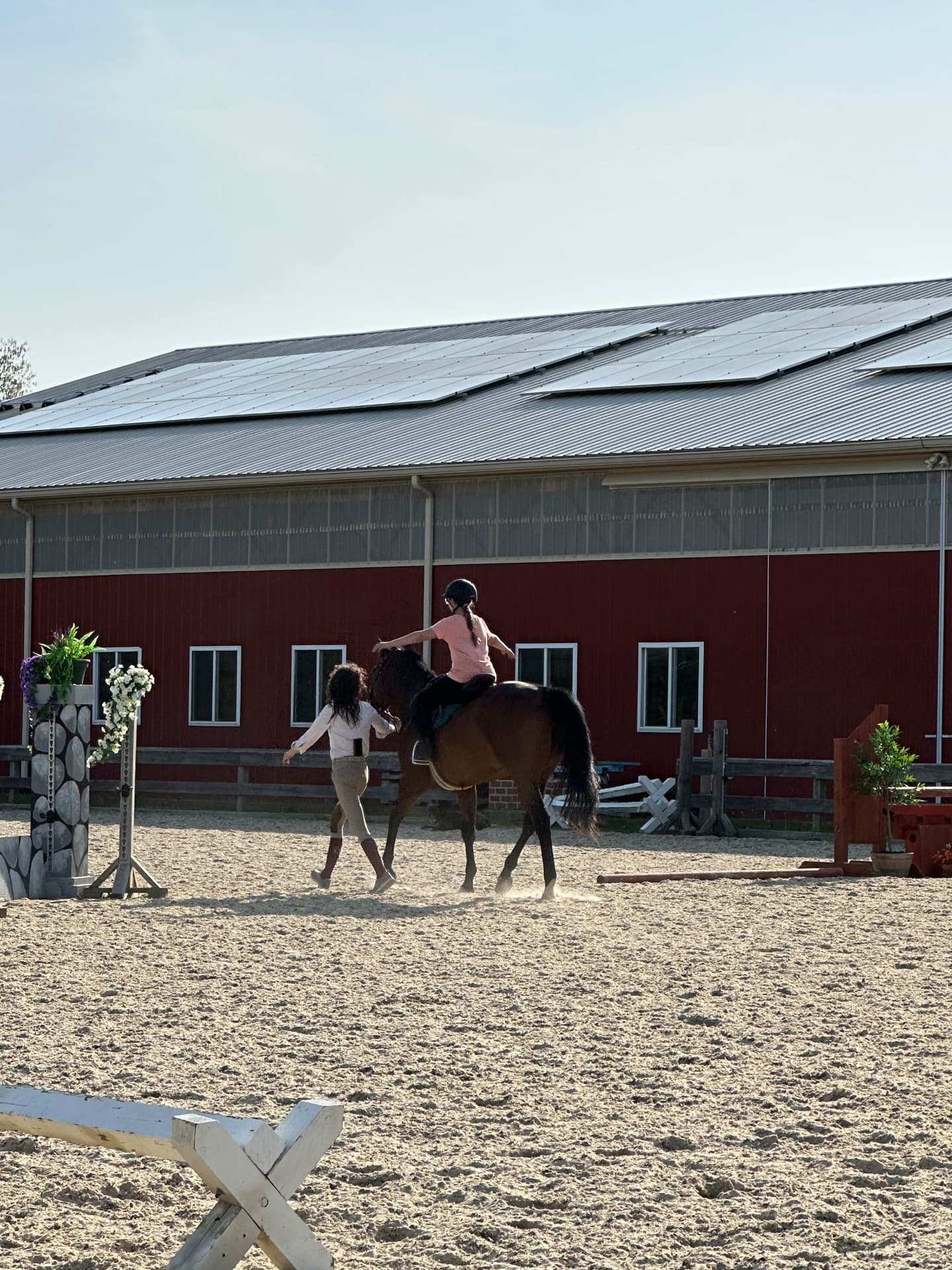 A helmeted rider practicing with arms extended on a bay horse while a person guides the horse in the Posnerosa outdoor arena