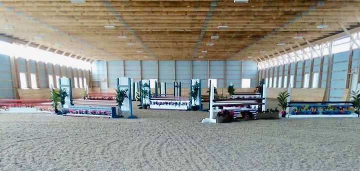 Interior of the Posnerosa indoor riding arena with sandy footing, colorful hunter-jumper fences and a timber ceiling